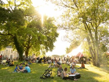 Des festivalier des Beaux Jours sont assis dans l'herbe devant l'un des chapiteaux