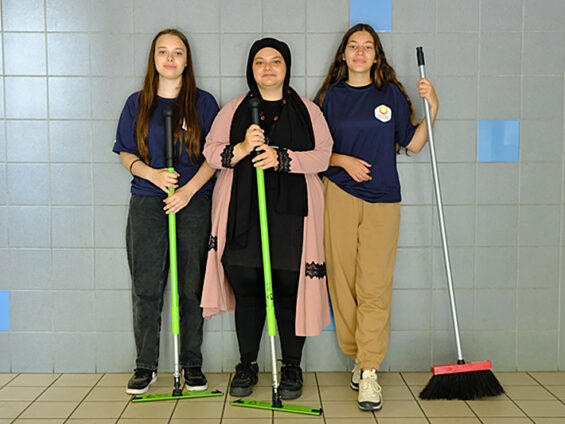 Trois jeunes de la coopérative posent avec des outils de ménage dans un hall d'immeuble