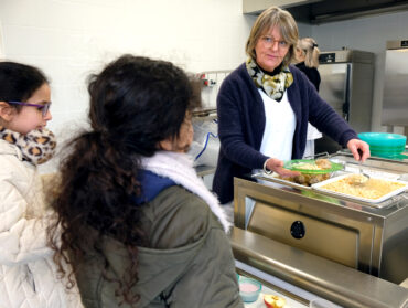Une agente de la restauration scolaire sert un plat à une enfant.