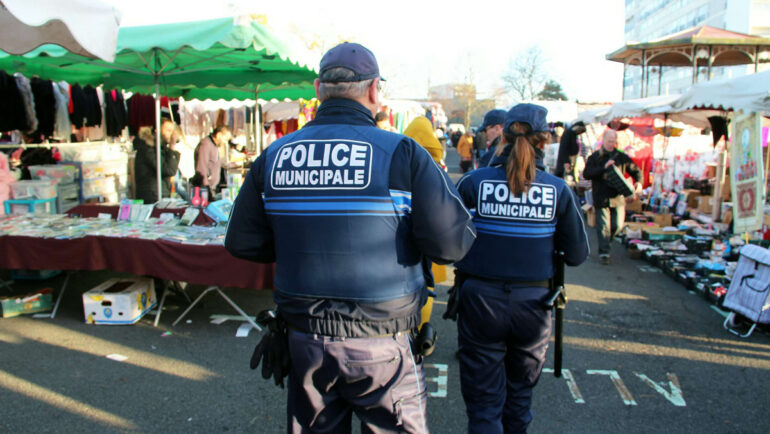 Deux policiers municipaux patrouillent au milieu des étals du marché de Bellevue. Il sont de dos.