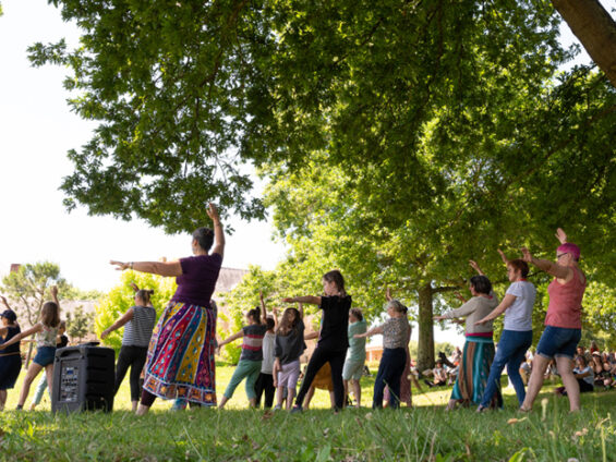 Un groupe de personnes fait un mouvement de danse indienne sous un arbre du parc de la Bégraisière.