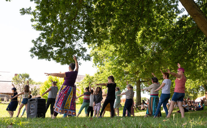 Un groupe de personnes fait un mouvement de danse indienne sous un arbre du parc de la Bégraisière.