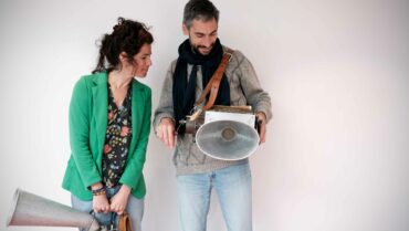 Les deux artistes posent devant un mur blanc leurs instruments à la main. Ils regardent tous les deux l'instrument de Sébastien Chevillard.