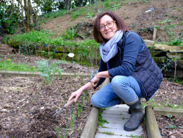 Cécile Durance accroupie devant un carré potager une binette à la main.