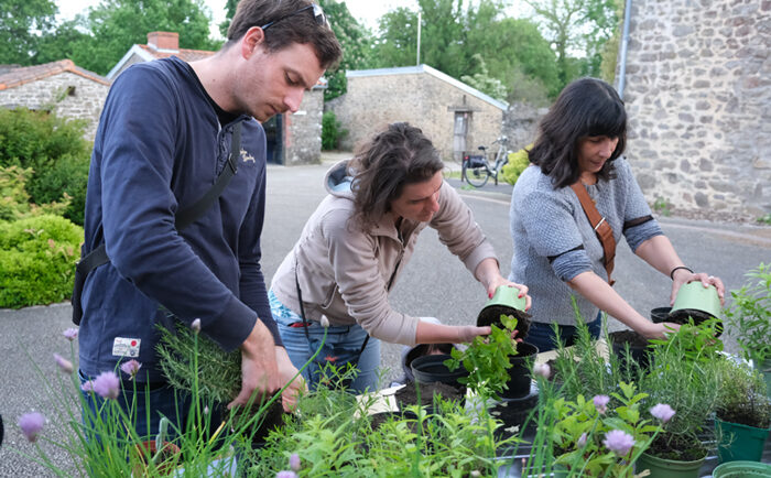 Trois personnes remportent des plantes sur une table devant la Longère.