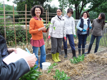 Annie Ardois est entourée de ces élèves devant un carré potager du jardin pédagogique de la Longère. Toutes sourient. On aperçoit les mains d'une personne qui tient un stylo et un cahier.