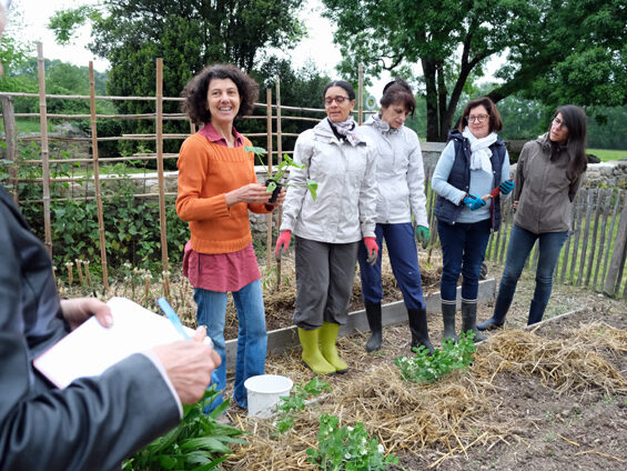 Annie Ardois est entourée de ces élèves devant un carré potager du jardin pédagogique de la Longère. Toutes sourient. On aperçoit les mains d'une personne qui tient un stylo et un cahier.