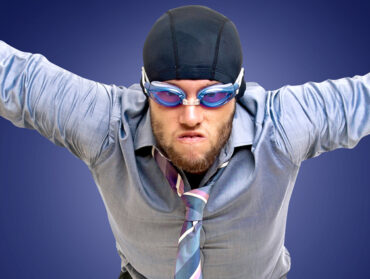 un homme en costume cravate portant des lunettes de piscine mime le fait de plonger face à nous
