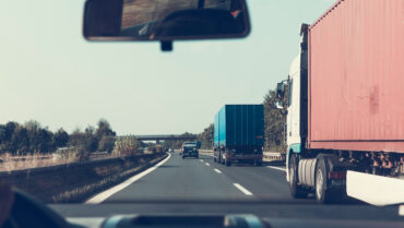 vue sur deux camions à travers le pare-brise d'une voiture en train de les dépasser sur un autoroute.