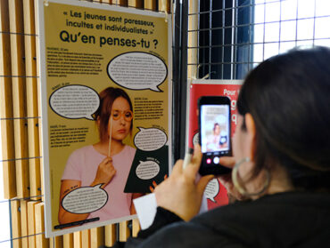 Une jeune femme prend en photo un panneau de l’exposition Paroles de jeunes.