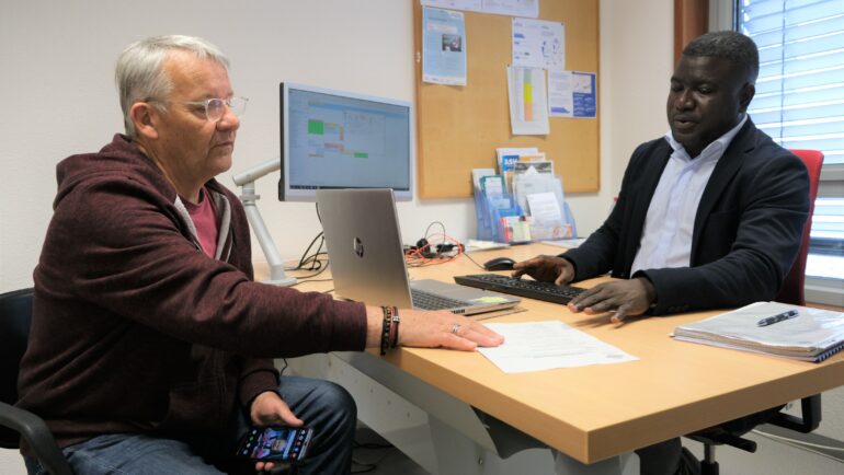 Un homme assis face un travailleur social du CCAS, lequel cherche des informations sur son ordinateur.