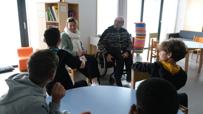 Des élèves sont face à un homme en fauteuil roulant, dans une salle de classe.