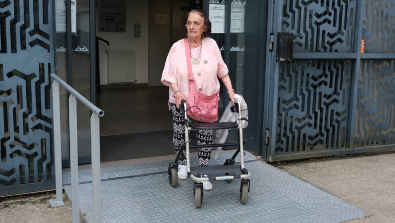 Une personne âgée en déambulateur emprunte la rampe d'accès d'un bâtiment public herblinois.