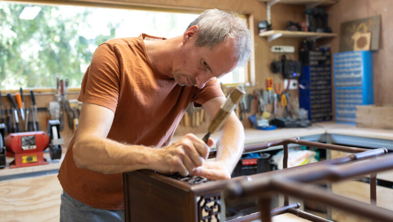 Un homme sculpte un tabouret en bois dans son atelier.