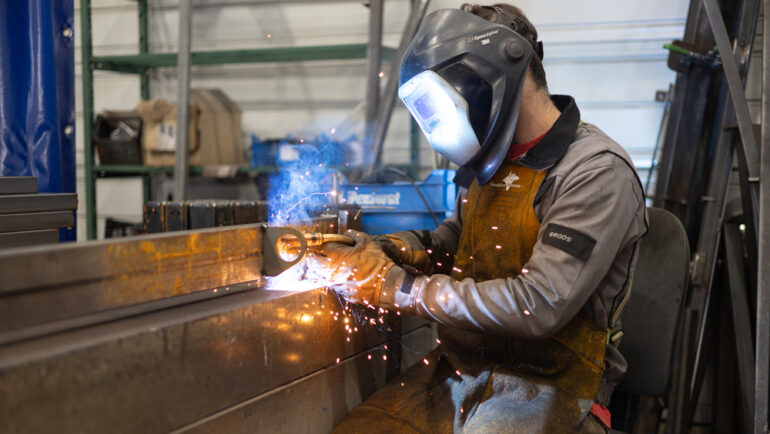 Gros plan sur un ouvrier casqué en train de souder une pièce de métal.
