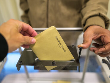 Une main s'apprête à glisser un bulletin de vote marqué 