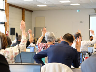 Elus de dos qui lèvent la main pour voter, dans la salle associative du Vigneua