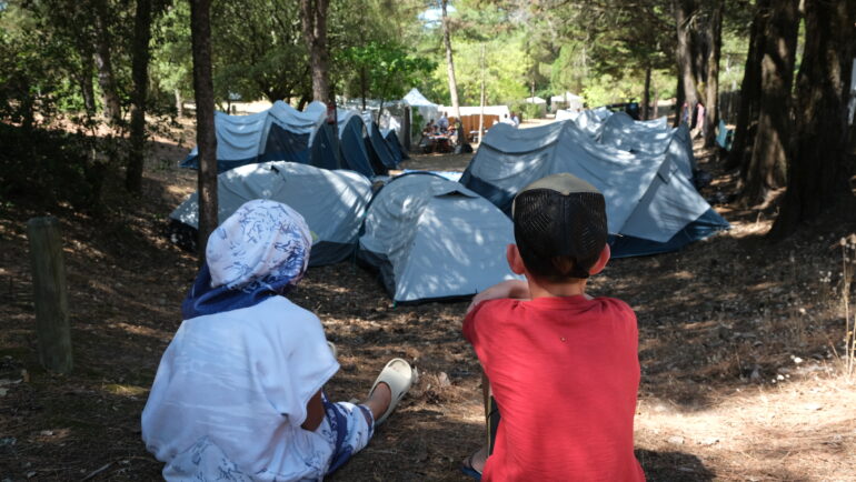 Deux jeunes garçons de dos regardent vers le campement de la colonie de vacances.