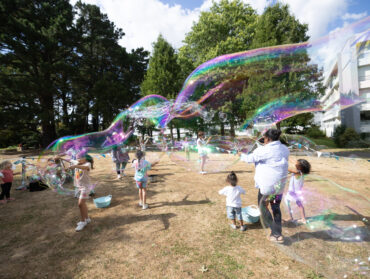Des enfants et des adultes s'amusent avec des bulles géantes dans le parc du Clos Fleuri